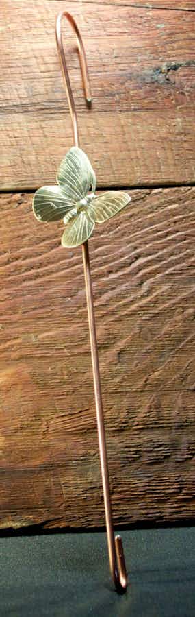 Copper coated extension hook with a brass butterfly leaning against wood