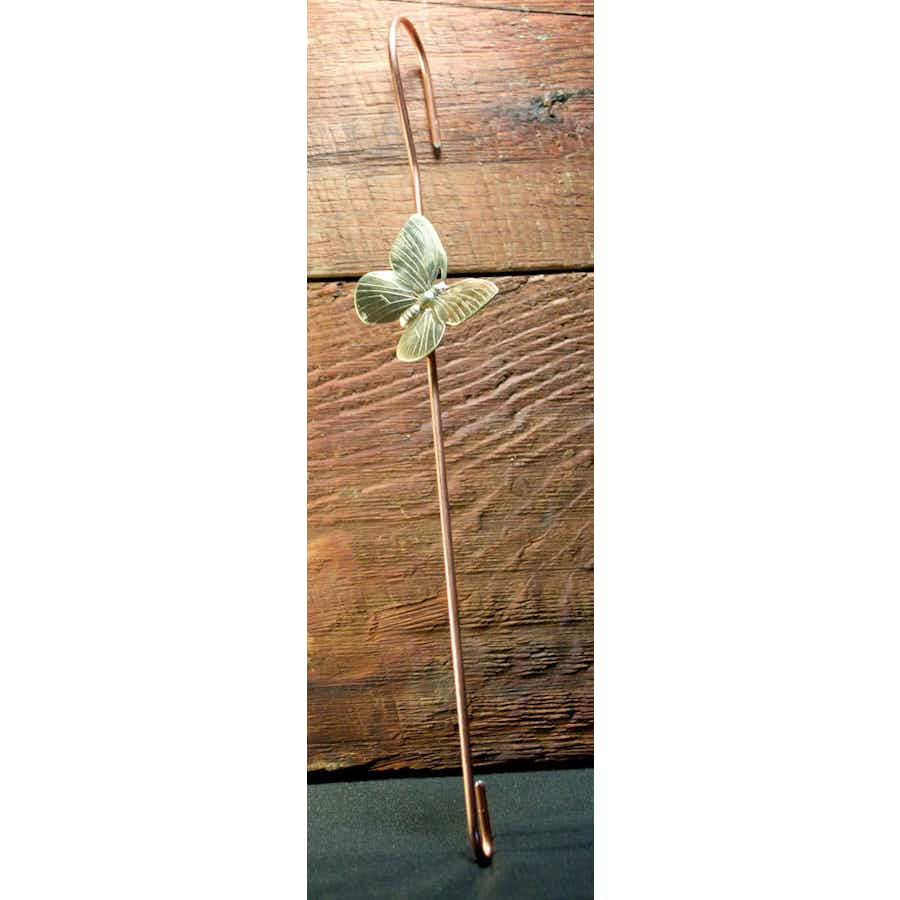 Copper coated extension hook with a brass butterfly leaning against wood
